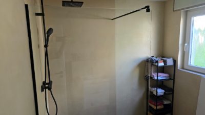 Bodengleiche Dusche mit fugenloser Mikrozement-Wand in Sandton, schwarzer Armatur und Glasabtrennung – fugenlose Badsanierung mit Mikrozement von mf.steintechnik aus Kirchheim am Neckar