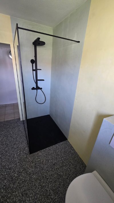 Walk-in-Dusche mit fugenloser Mikrozement-Wand in Grau, schwarzer Regenbrause und dunkler Duschtasse – fugenlose Badsanierung mit Mikrozement von mf.steintechnik aus Kirchheim am Neckar