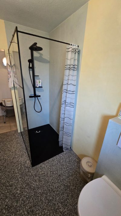 Dusche mit fugenloser Mikrozement-Wand, schwarzer Regenbrause und grauem Steinteppich-Boden – fugenlose Badsanierung mit Mikrozement von mf.steintechnik aus Kirchheim am Neckar