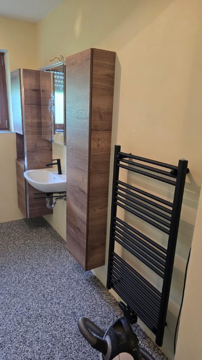 Badezimmer mit grauem Steinteppich-Boden, Waschtisch in Holzoptik und schwarzem Handtuchheizkörper – Badsanierung von mf.steintechnik aus Kirchheim am Neckar