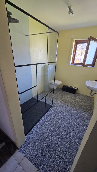 Badezimmer mit dunklem Steinteppich-Boden und Duschabtrennung mit schwarzem Rahmen – Badsanierung von mf.steintechnik aus Kirchheim am Neckar